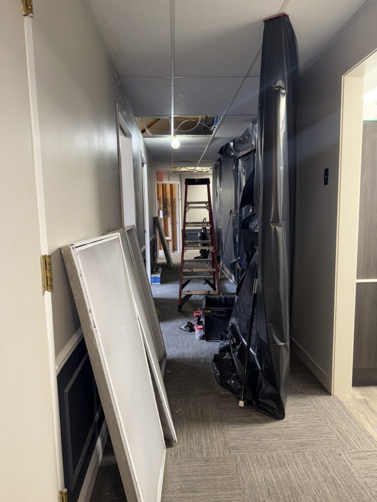 A hallway under renovation with a ladder, a black plastic barrier, and removed ceiling panels.