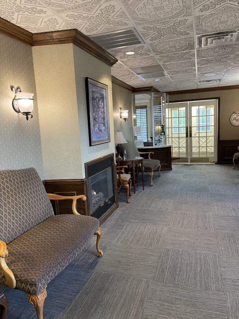 A waiting area with patterned armchairs, a fireplace, and a reception desk leading to a glass-paned double door.